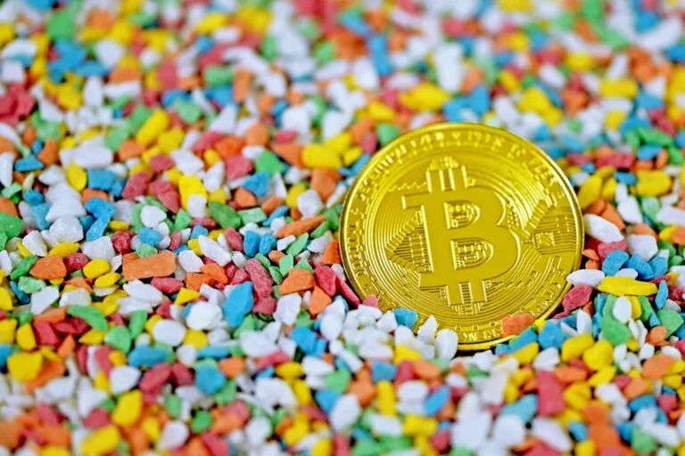 Złota moneta Bitcoin leży na kolorowych cukierkach