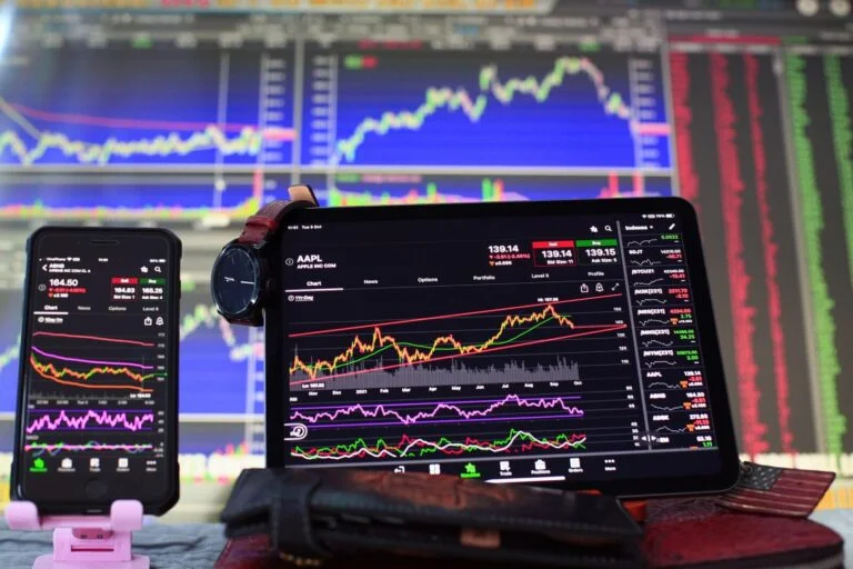 Smartfon i tablet wyświetlające wykresy handlowe AAPL na tle monitora z analizą giełdową