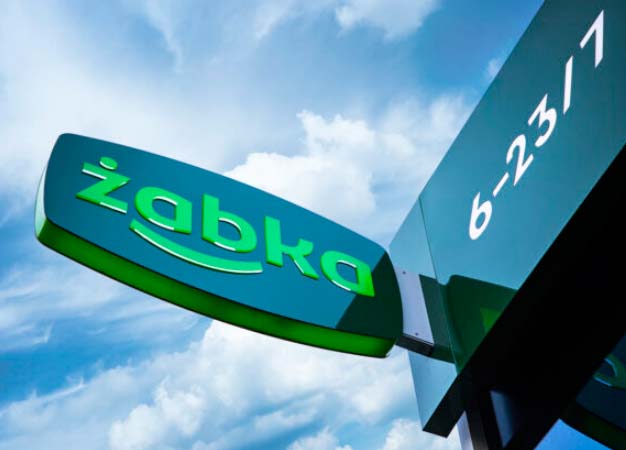 Zielony neon Żabki na szyldzie sklepu na tle nieba